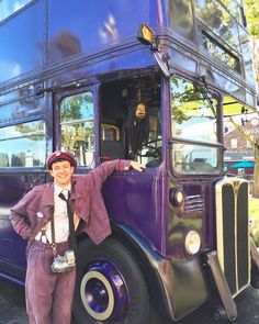 a man standing in front of a purple double decker bus with his hands on the door