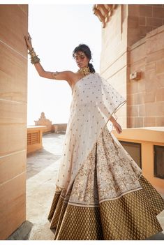 a woman in a white and gold lehenga standing on the side of a building