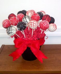 a black vase filled with red and white chocolate covered lollipops on top of a wooden table