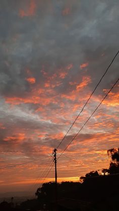 the sun is setting behind power lines and telephone poles in the foreground, with trees to the side