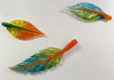 three colorful glass leaves sitting on top of a white table