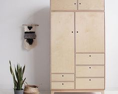 a wooden cabinet sitting next to a potted plant on top of a white floor