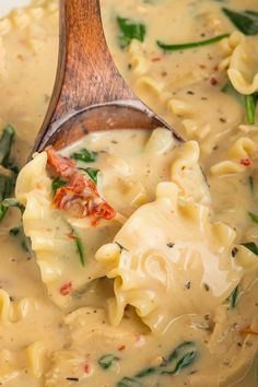 a wooden spoon filled with pasta and spinach in a creamy broccoli sauce