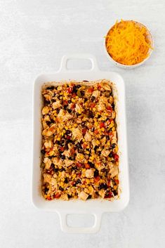 a casserole dish filled with chicken and vegetables next to a bowl of shredded cheese