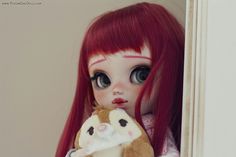 a doll with long red hair holding a stuffed animal in her hand and looking at the camera