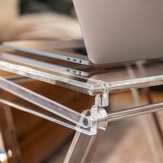 a laptop computer sitting on top of a clear shelf next to a glass table and chair