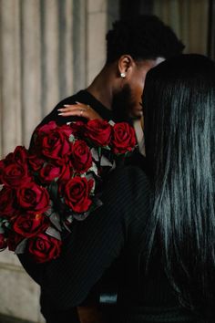 a man holding a bouquet of red roses next to a woman with long black hair