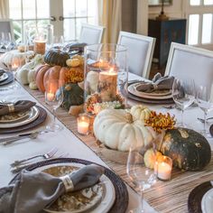 a table set with pumpkins, candles and plates