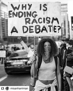 a woman holding a sign that says why is ending racism a debate?