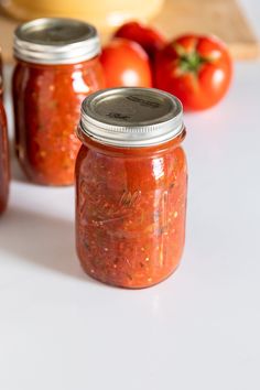 three jars filled with food sitting on top of a white counter next to tomatoes and cheese