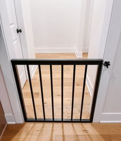 an open door with a black railing in the middle of a wooden floor and white walls