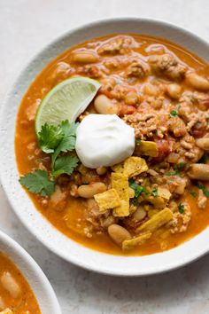 a white bowl filled with beans and tortilla soup next to a lime wedge