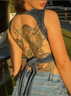 a woman with tattoos on her back standing in front of a bench and looking off to the side