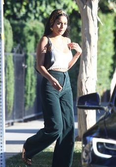 a woman is walking down the street with her hand on her hip and wearing green pants