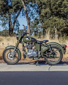 a green motorcycle parked on the side of a road next to some grass and trees