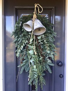 a door with a wreath and bells hanging from it's front door, decorated with greenery