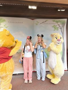 two girls are standing next to winnie the pooh and her friends in front of an open book