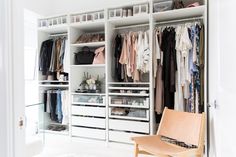 a white closet filled with lots of clothes and shoes next to a wooden chair on top of a hard wood floor