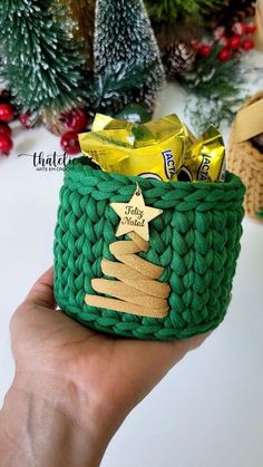 a hand holding a green knitted basket with gold foil christmas tree decorations on it