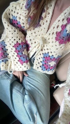 a woman sitting on top of a couch wearing a crocheted sweater and jeans