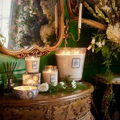 candles and flowers are sitting on a table in front of a mirror with an ornate frame