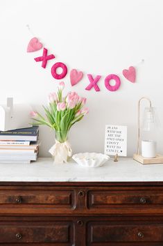 a vase with pink flowers sitting on top of a dresser next to a sign that says xoxo