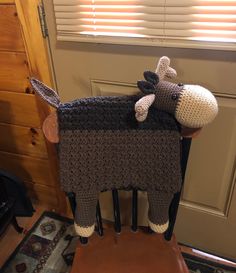 a crocheted cow sitting on top of a wooden chair next to a window