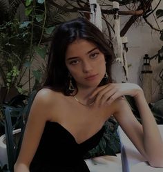 a woman in a black dress is sitting on a white chair and posing for the camera