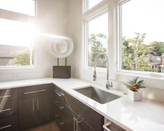 a kitchen with two windows and a sink in front of the window is sun shining through