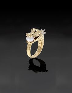 a gold ring with an alligator head and pearls on the side, against a black background