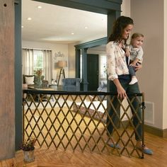 a woman holding a baby standing on top of a wooden floor next to a living room