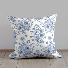 a blue and white floral pillow sitting on top of a wooden floor next to a gray wall