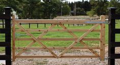 an open wooden gate in the middle of a field with trees and grass behind it