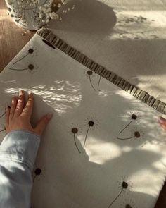 a person's hand is on the edge of a piece of fabric that has dandelions on it