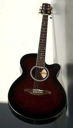 an acoustic guitar hanging on the wall in front of a white wall with shadow from it