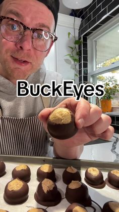 a man holding up a chocolate covered cookie in front of a baking tray with cookies on it