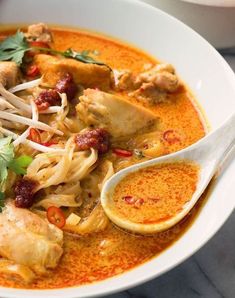 a white bowl filled with chicken and noodle soup next to a spoon on a table