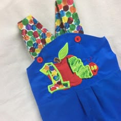 a child's blue dress with an apple and caterpillar applique on it