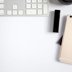 an iphone, camera and keyboard on a white surface with the phone in front of it