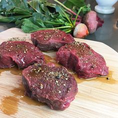 four raw steaks on a cutting board with herbs and garlic sprinkled over them