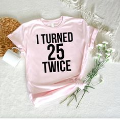 a pink shirt that says i turned 25 twice next to some flowers and a wicker basket