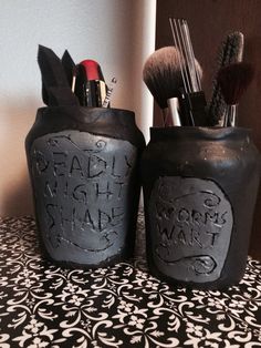 two black jars with makeup brushes in them