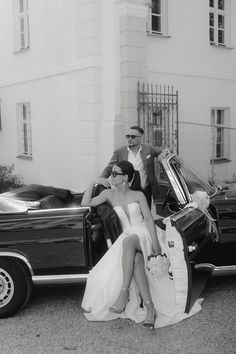 a man and woman sitting on the back of a car next to each other in front of a building