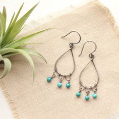 "Forged silver teardrops have been uniquely wrapped with wire to create chandelier style earrings. Little drops of deep turquoise dangle from the hand formed loops. Delicate but not shy. Handmade shepherd hook earwires. Measure 2\". Sterling silver, which has been oxidized and hand polished for an antique finish. About Turquoise: The name turquoise means \"Turkish stone\" because the trade route that brought it to Europe came via Turkey. Turquoise is a non-translucent stone of which the most val Teardrop Chandelier Earrings For Jewelry Making, Turquoise Teardrop Chandelier Earrings As Gift, Hypoallergenic Teardrop Chandelier Earrings, Turquoise Teardrop Chandelier Earrings For Pierced Ears, Green Teardrop Chandelier Earrings Nickel Free, Turquoise Drop Chandelier Earrings With Ear Wire, Handmade Turquoise Metal Chandelier Earrings, Turquoise Wire Wrapped Teardrop Earrings, Turquoise Teardrop Earrings Wire Wrapped