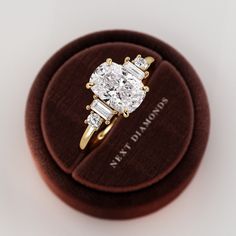 an oval diamond ring with three baguettes sits on top of a velvet box