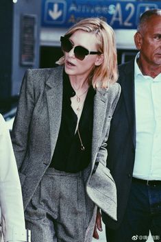 a woman walking down the street in a suit and sunglasses