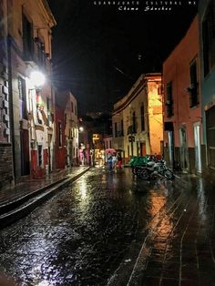 an empty street at night with people walking on the sidewalk and one person holding an umbrella