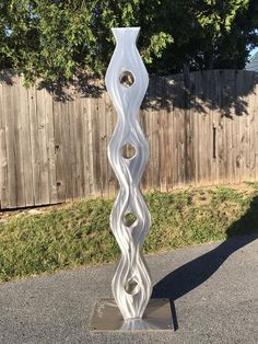 a tall white vase sitting on top of a metal stand in front of a fence