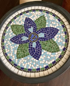 a round mosaic table with blue, green and white flowers on it's side