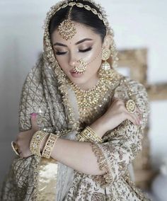 a woman in a bridal outfit with jewelry on her head and hands around her neck